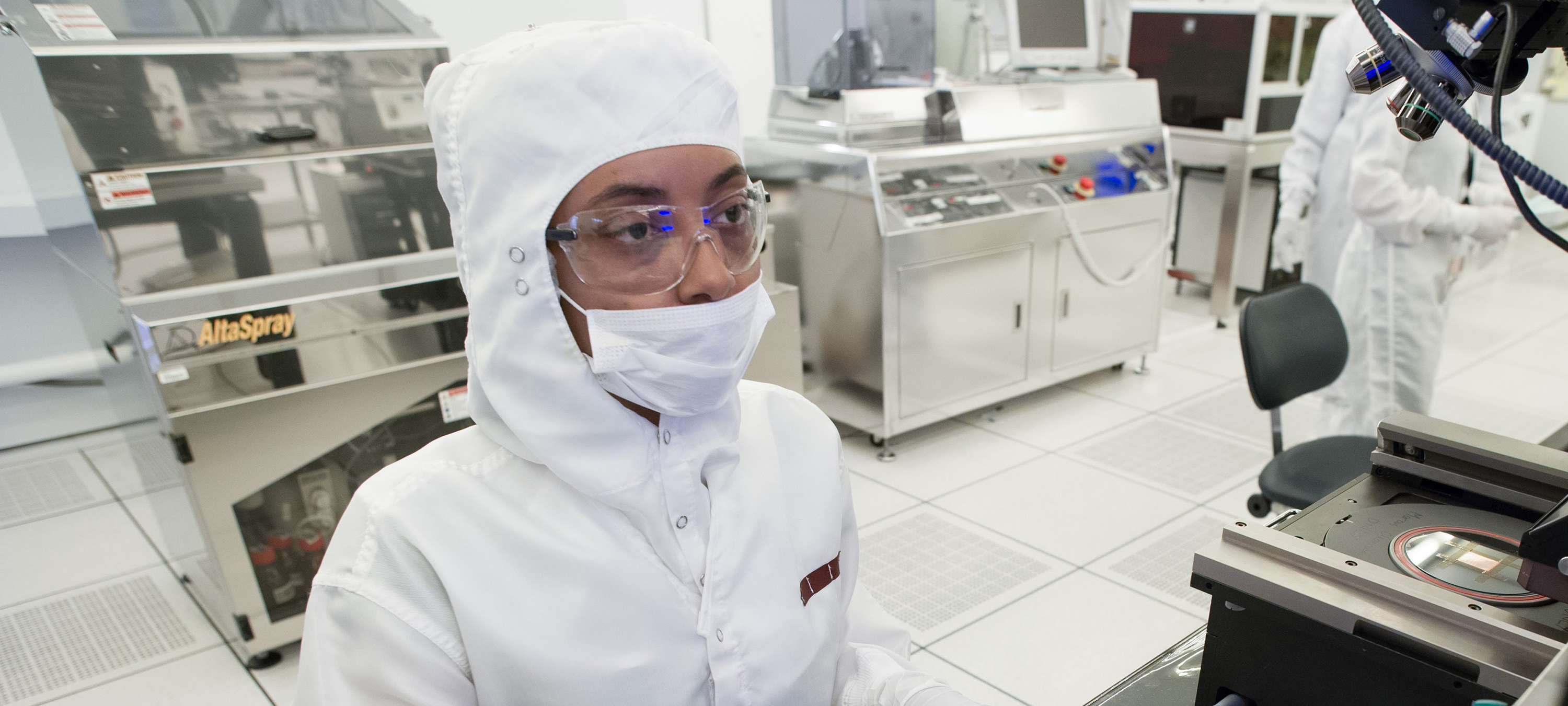 student sitting while working on a computer in a clean lab